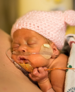 Portrait of a newborn baby wearing a knitted pink cap in an ICU hospital.